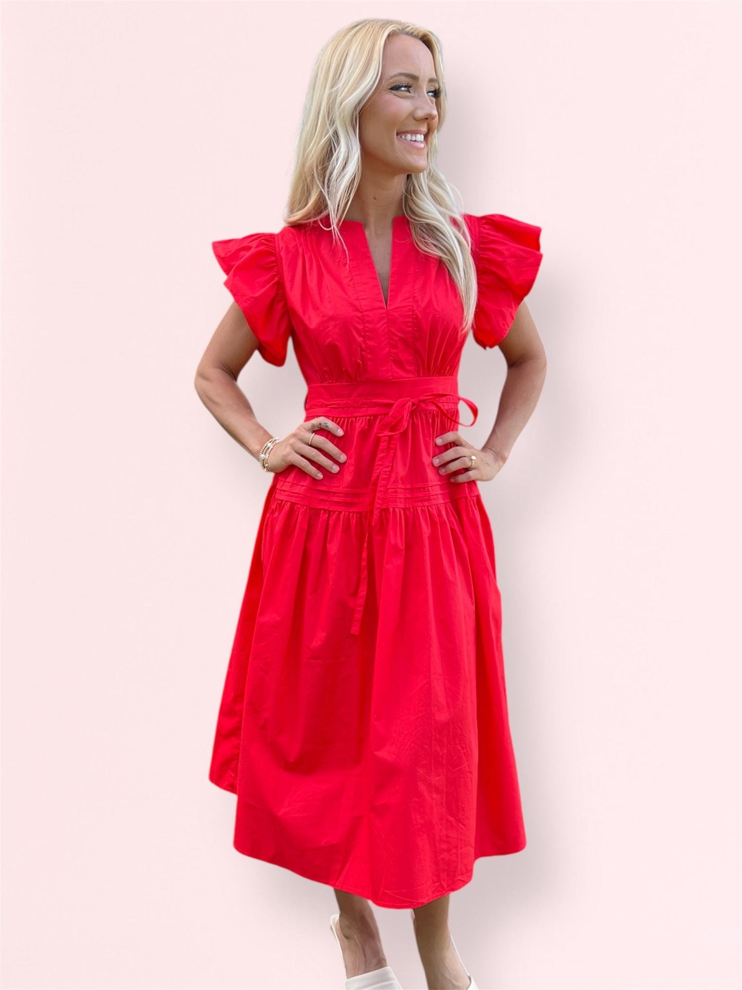 Woman modeling the Cala Midi Dress in red with her hands on hips and a big smile