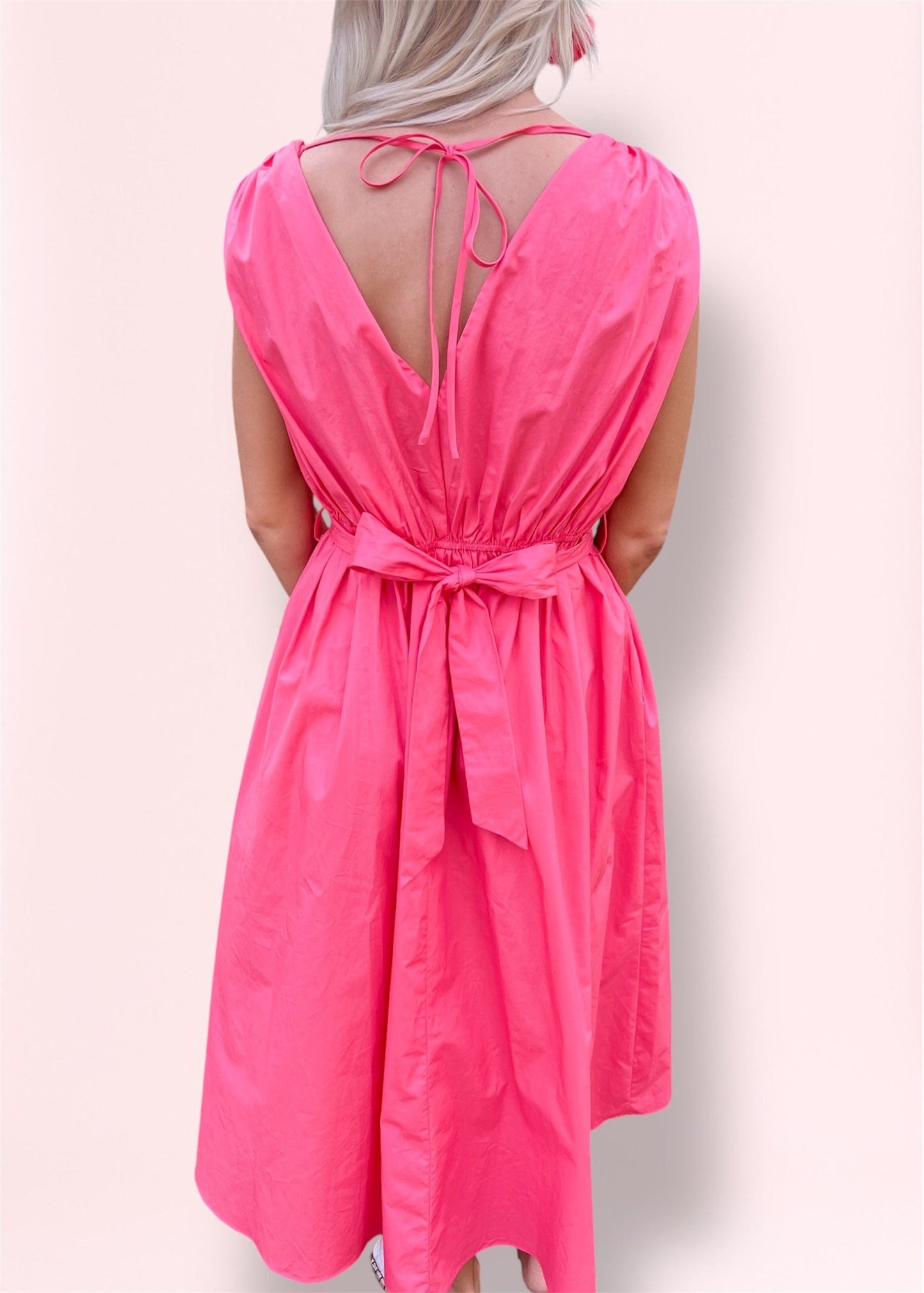 Back view of the Ilona Coral Midi Dress showcasing tie-back detail, adjustable waist with fabric bow, and lightweight, breezy material ideal for warm-weather wear.