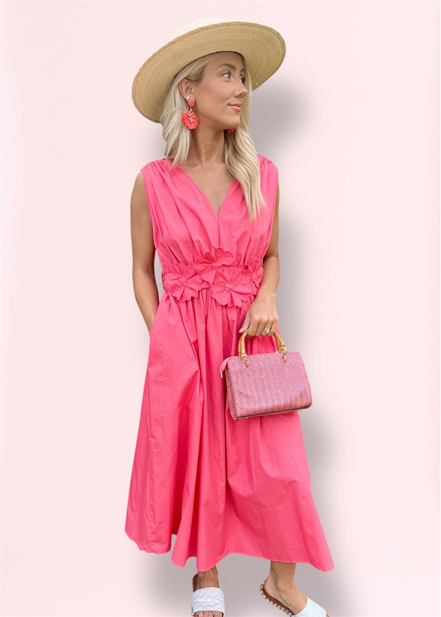 Model wearing the Ilona Coral Midi Dress styled with statement earrings, straw hat, and bamboo-handle woven pink handbag, perfect for spring and summer outings.