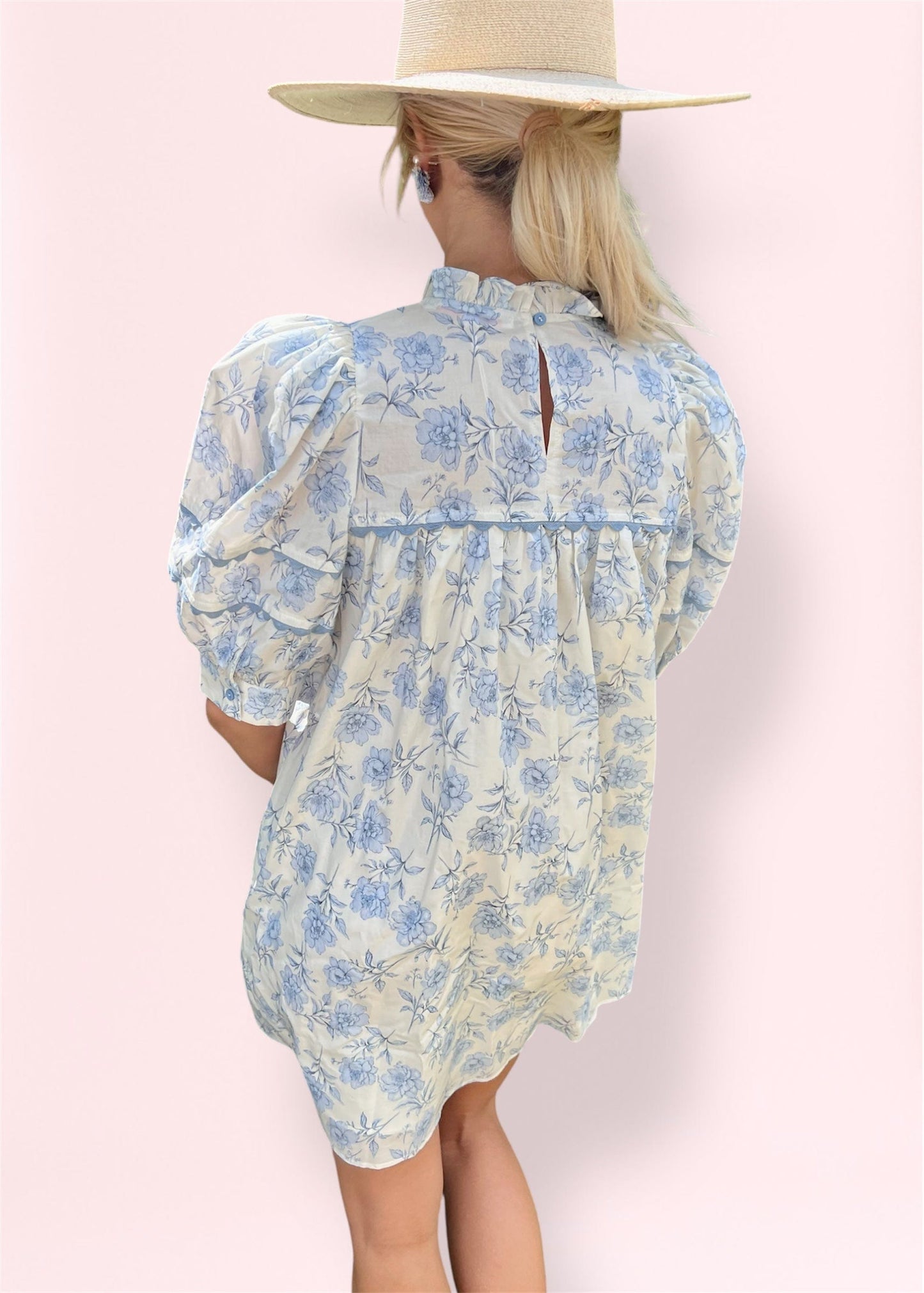 Back view of the floral babydoll dress featuring a keyhole button closure, gathered back detail, and puff sleeves, styled with a straw hat for a breezy, feminine look.