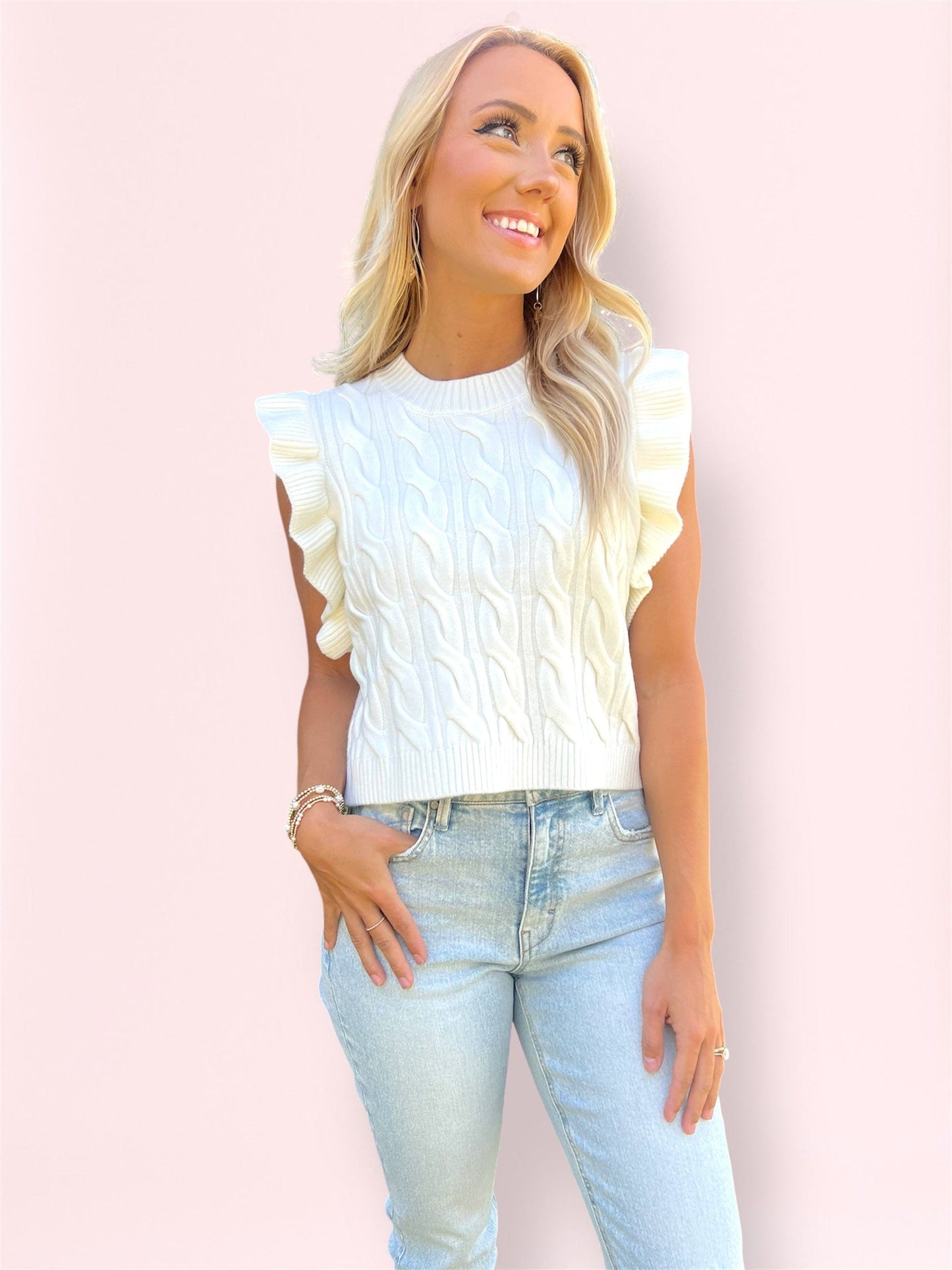 Close-up of woman wearing the ivory Miranda Vest with ruffle sleeves and cable knit detail, smiling and looking left