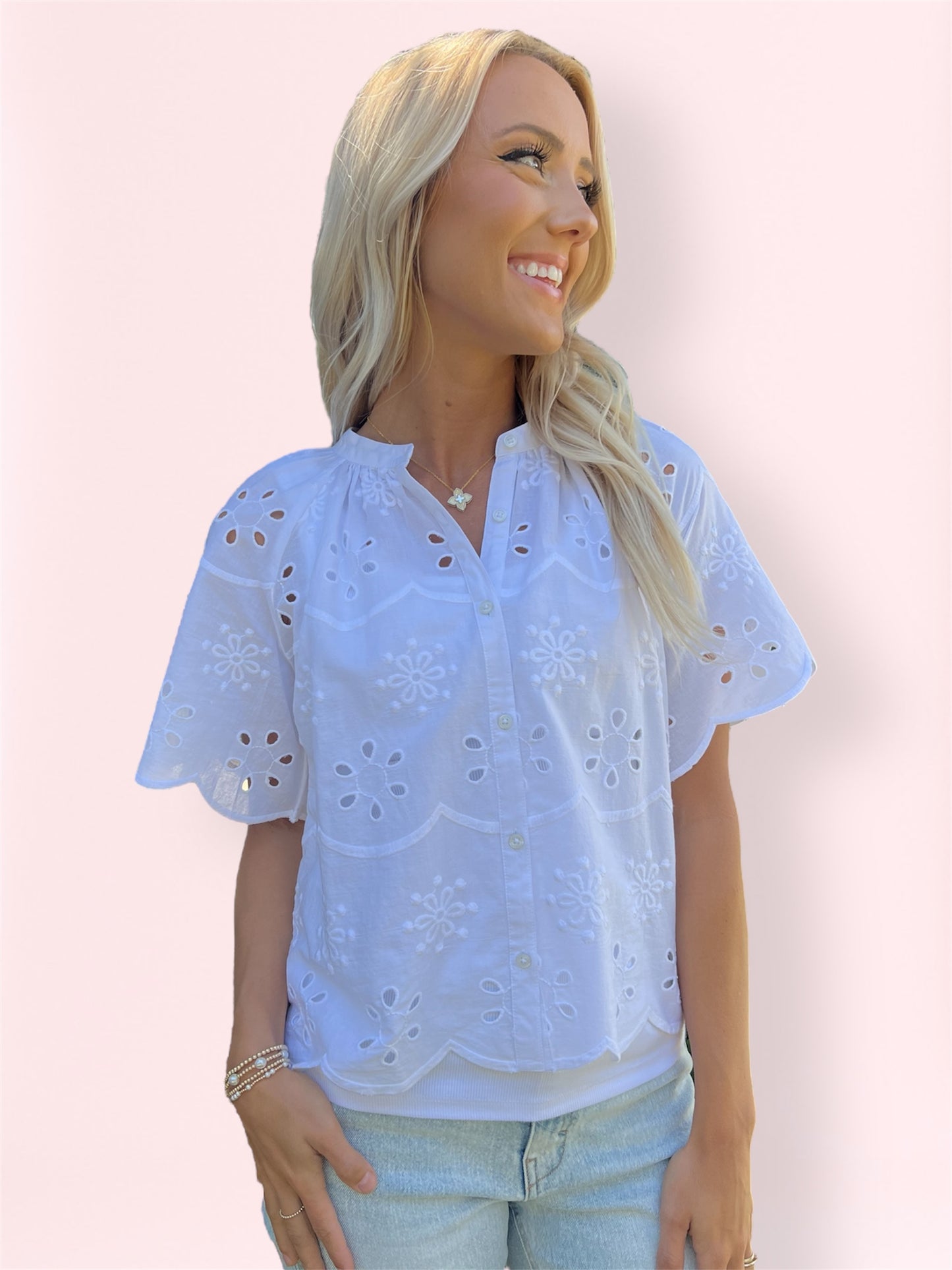 Woman wearing white eyelet embroidered blouse with scalloped sleeves and button-up front