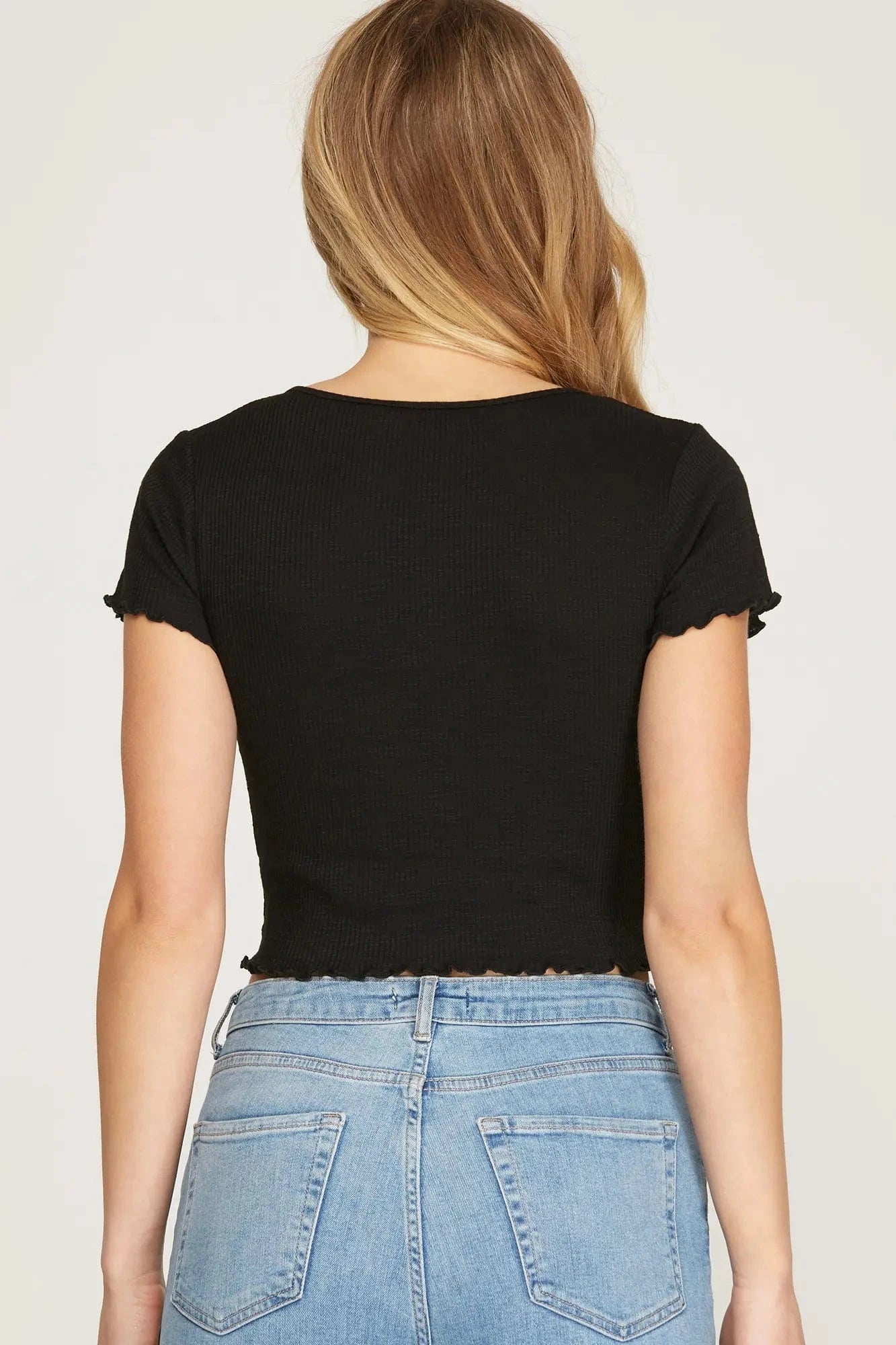 Back view of black ribbed crop top with short sleeves and lettuce hem