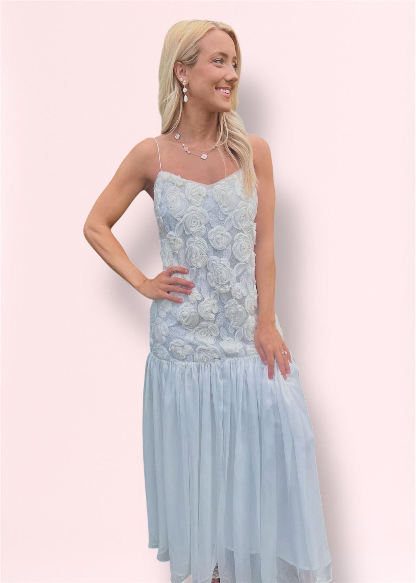 Side view of blonde woman wearing elegant white maxi dress with floral detailing and thin straps, styled for special occasions.