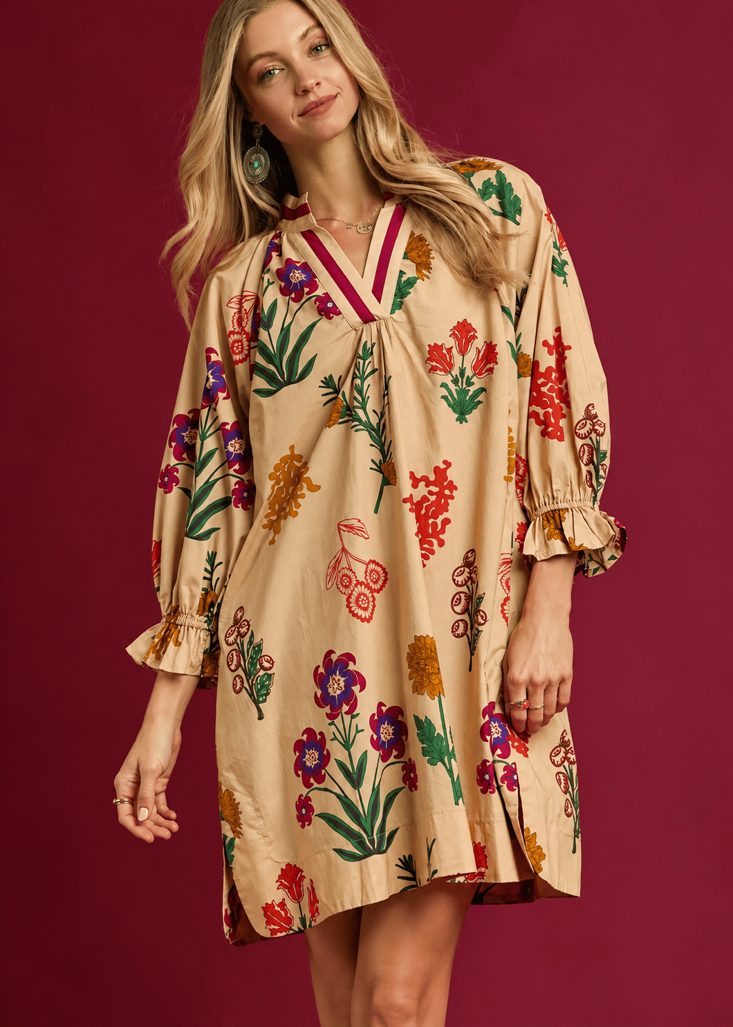 Model wearing tan multicolor floral shift dress with burgundy V-neck trim and ruffle sleeves.