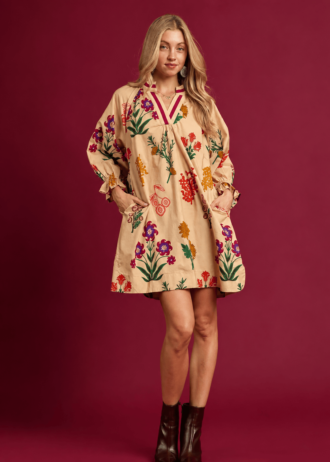 Tan floral mini shift dress with colorful botanical print, side pockets, and burgundy ankle boots.