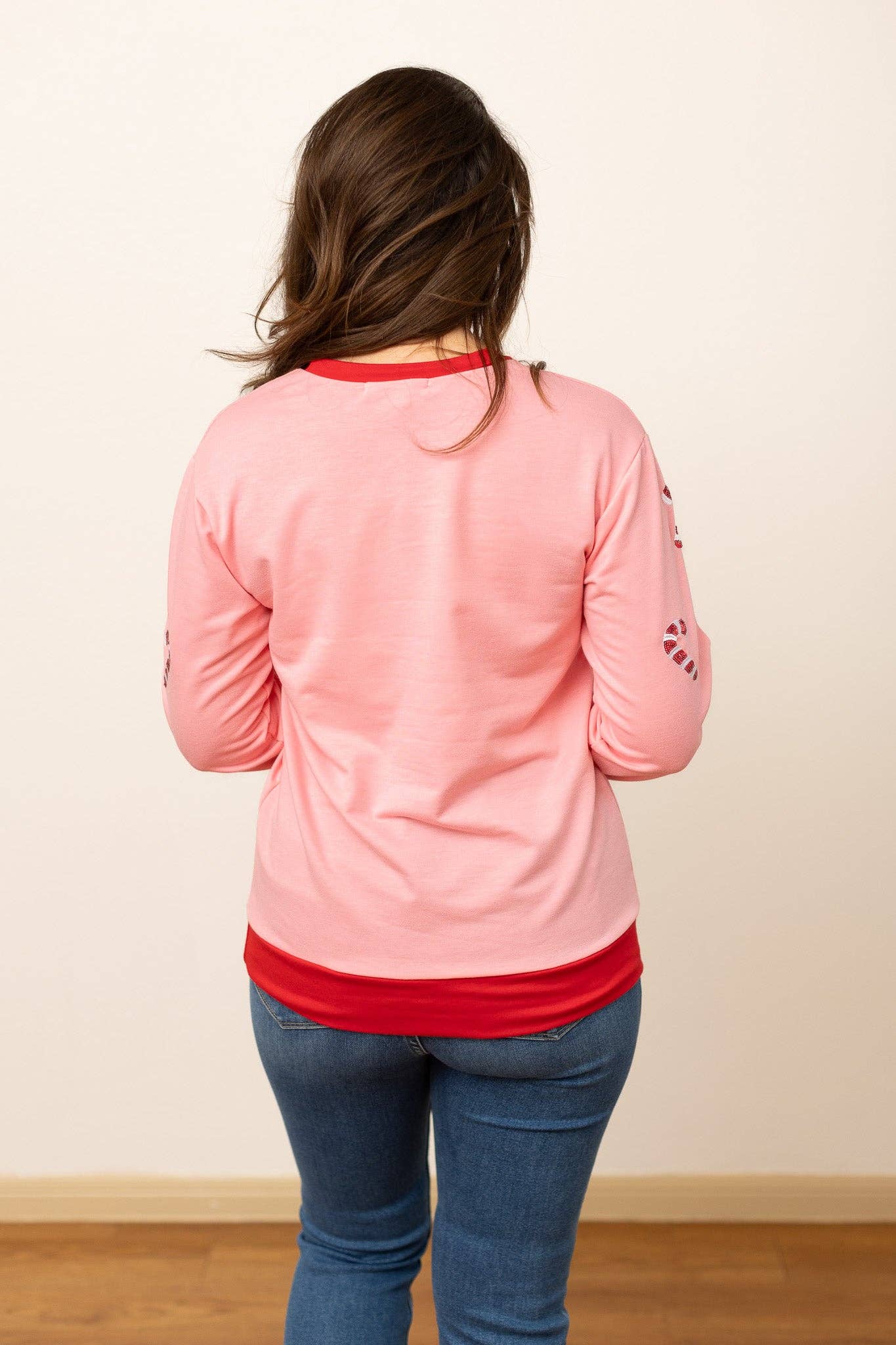 Back view of relaxed-fit pink holiday sweater with red collar and waistband