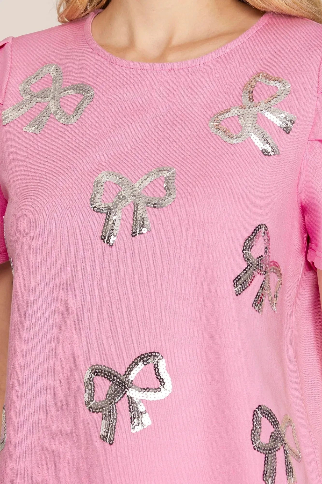 Close-up of silver sequin bow embellishments on pink short sleeve top