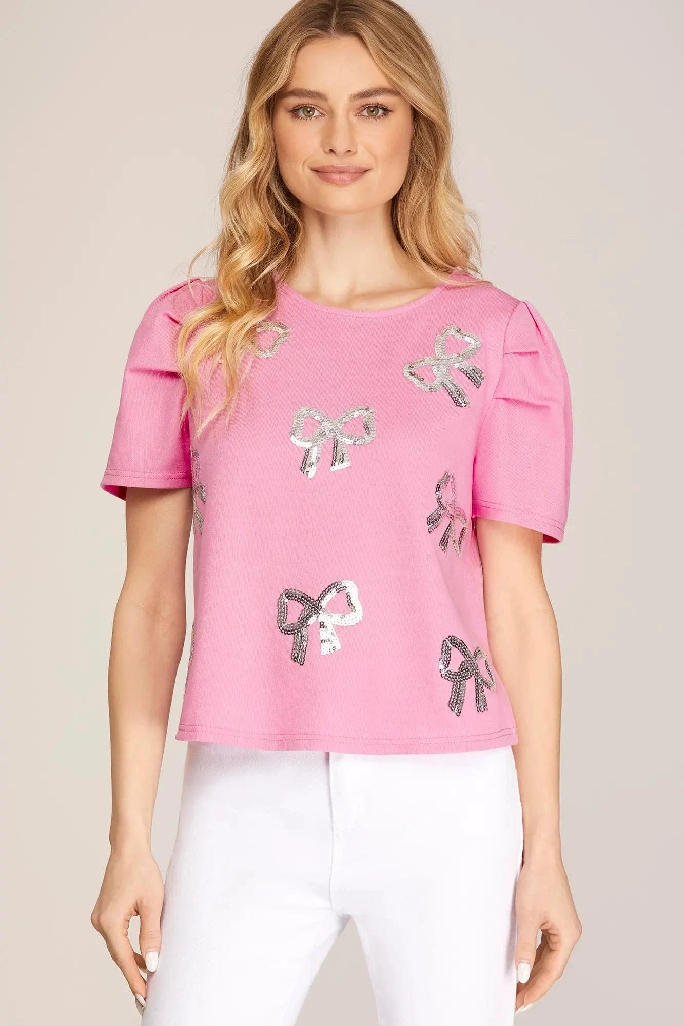 Barbie pink puff sleeve top with silver sequin bows, styled with white pants