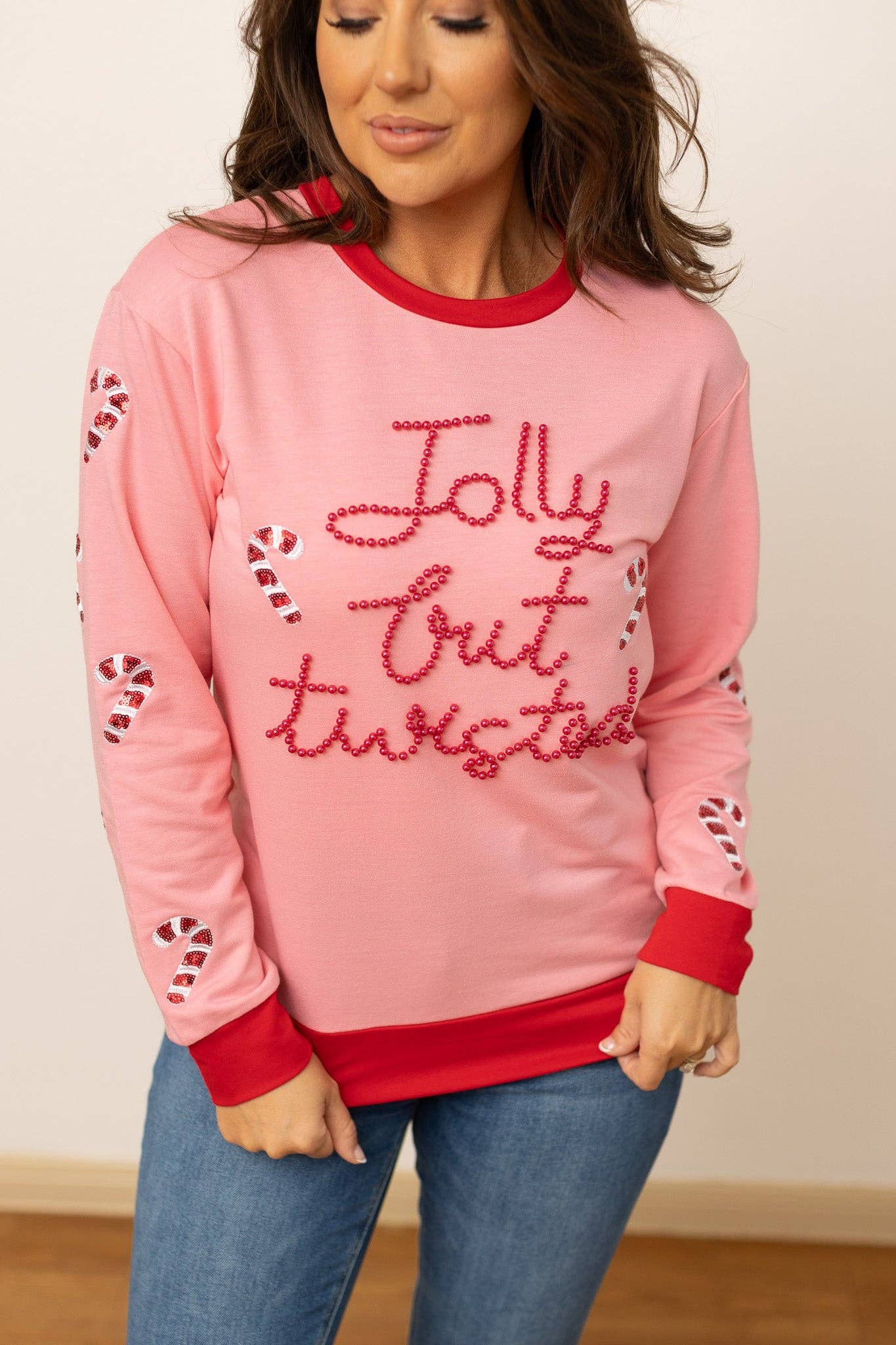 Close-up of Jolly but Twisted pink holiday sweatshirt with candy cane details and bead lettering