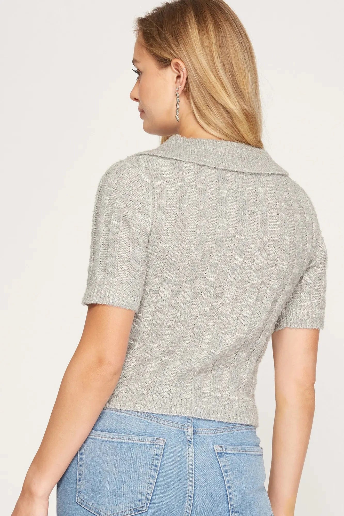 Back view of woman wearing a grey collared short sleeve ribbed sweater top, styled with high-waisted jeans for a cozy fall look
