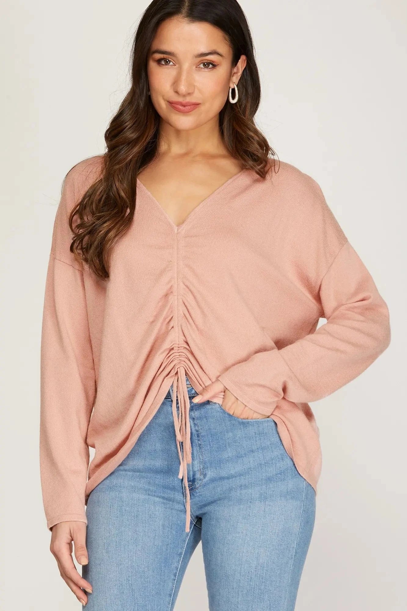 Model wearing blush pink front drawstring sweater with v-neck and ruched detailing.