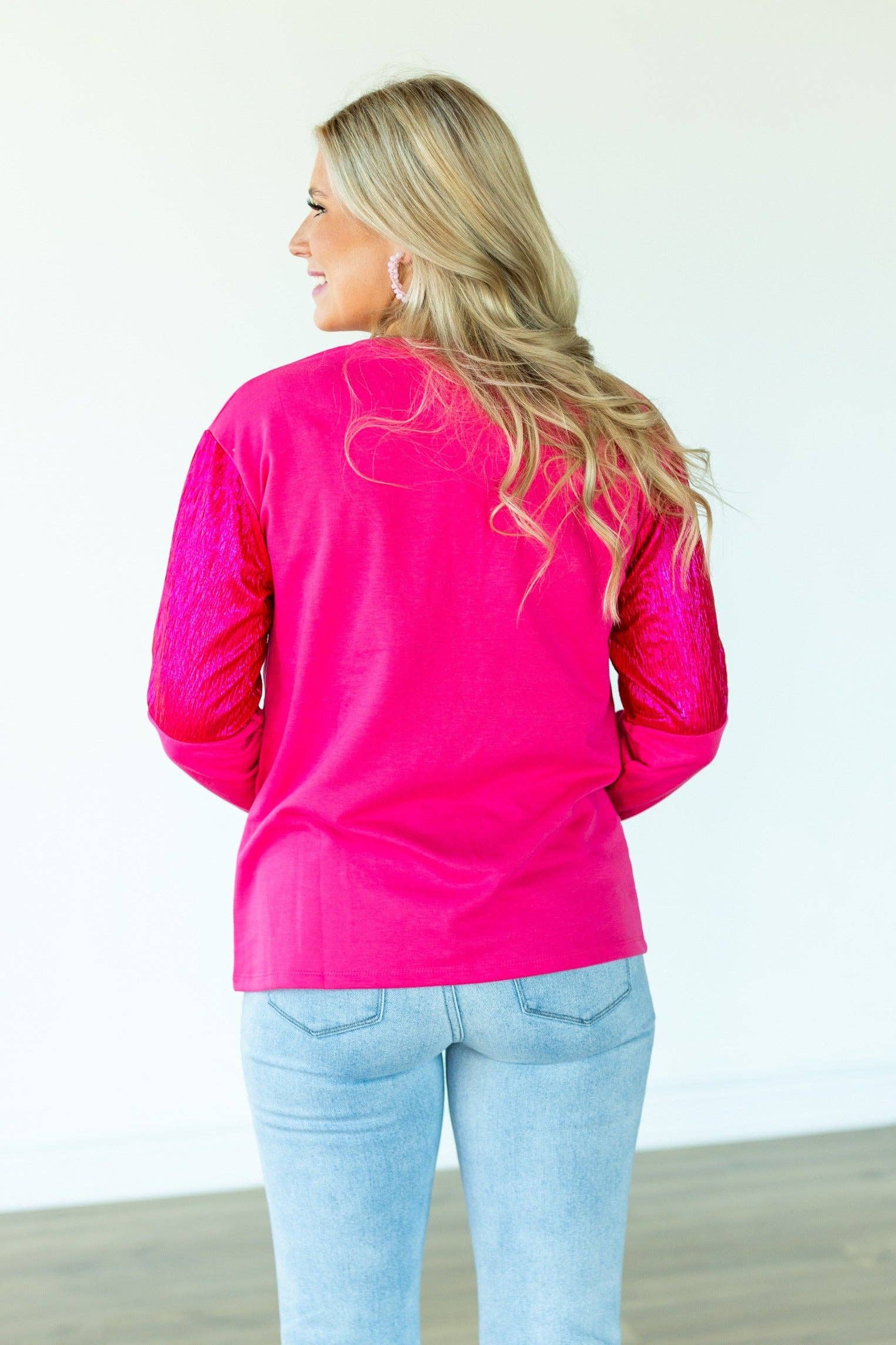Woman wearing a bright pink long-sleeve top with a heart design on the back, standing against a white background.