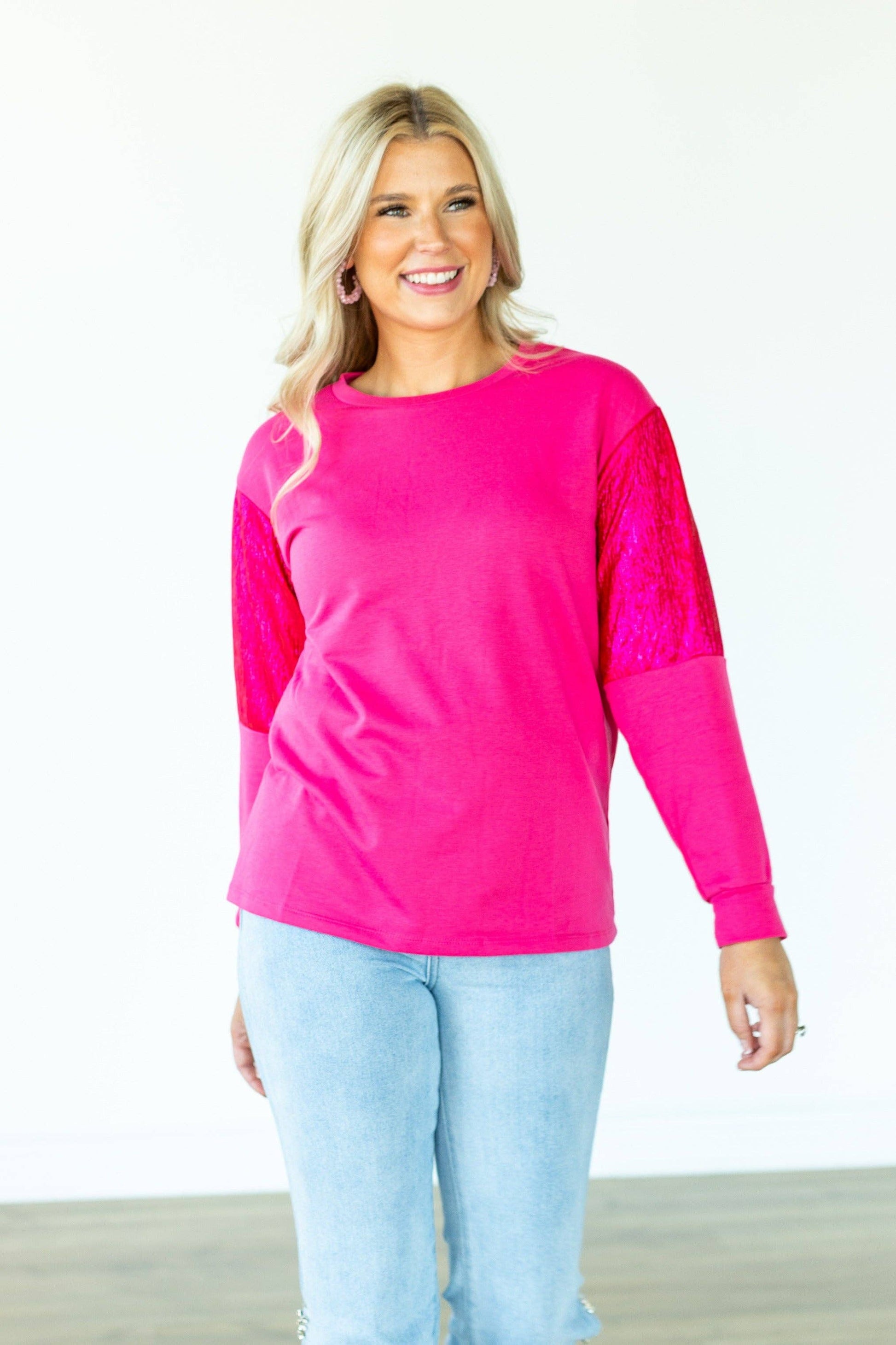 Woman wearing a bright pink long-sleeve top and light blue jeans on a white background