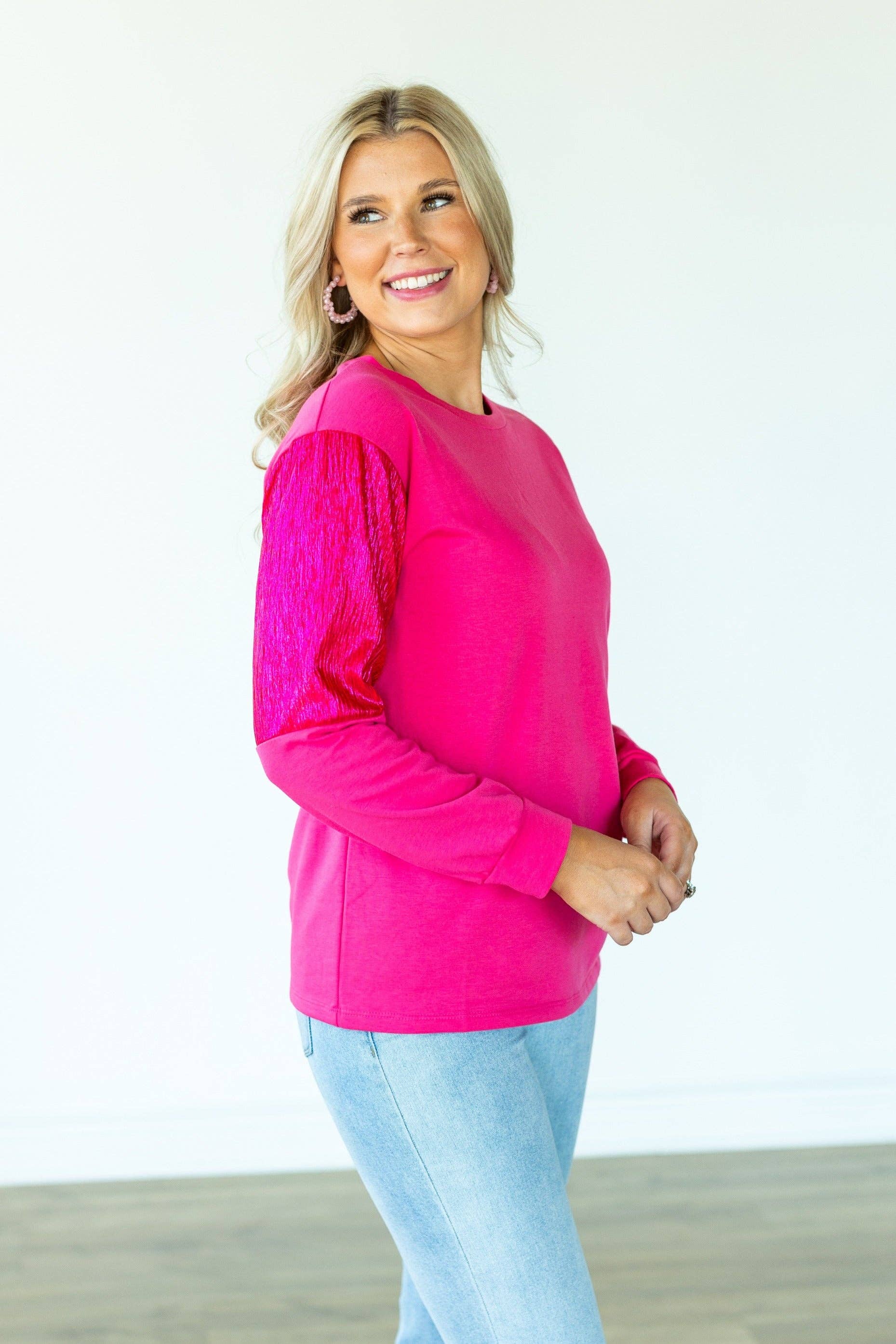 Woman wearing a bright pink top and light blue jeans against a white background