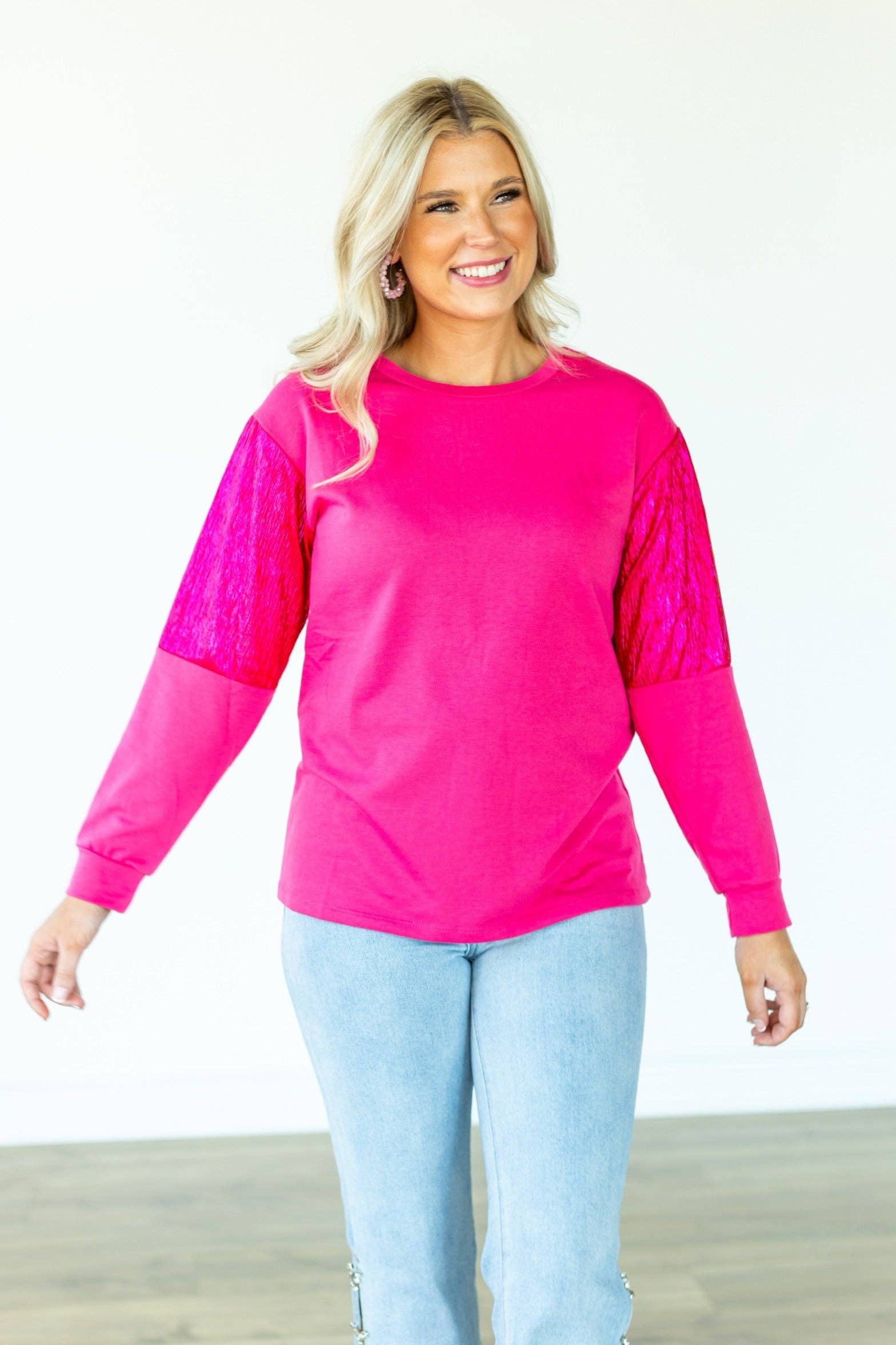 Woman wearing a bright pink long-sleeve top with a textured pattern on one sleeve, standing against a white background.