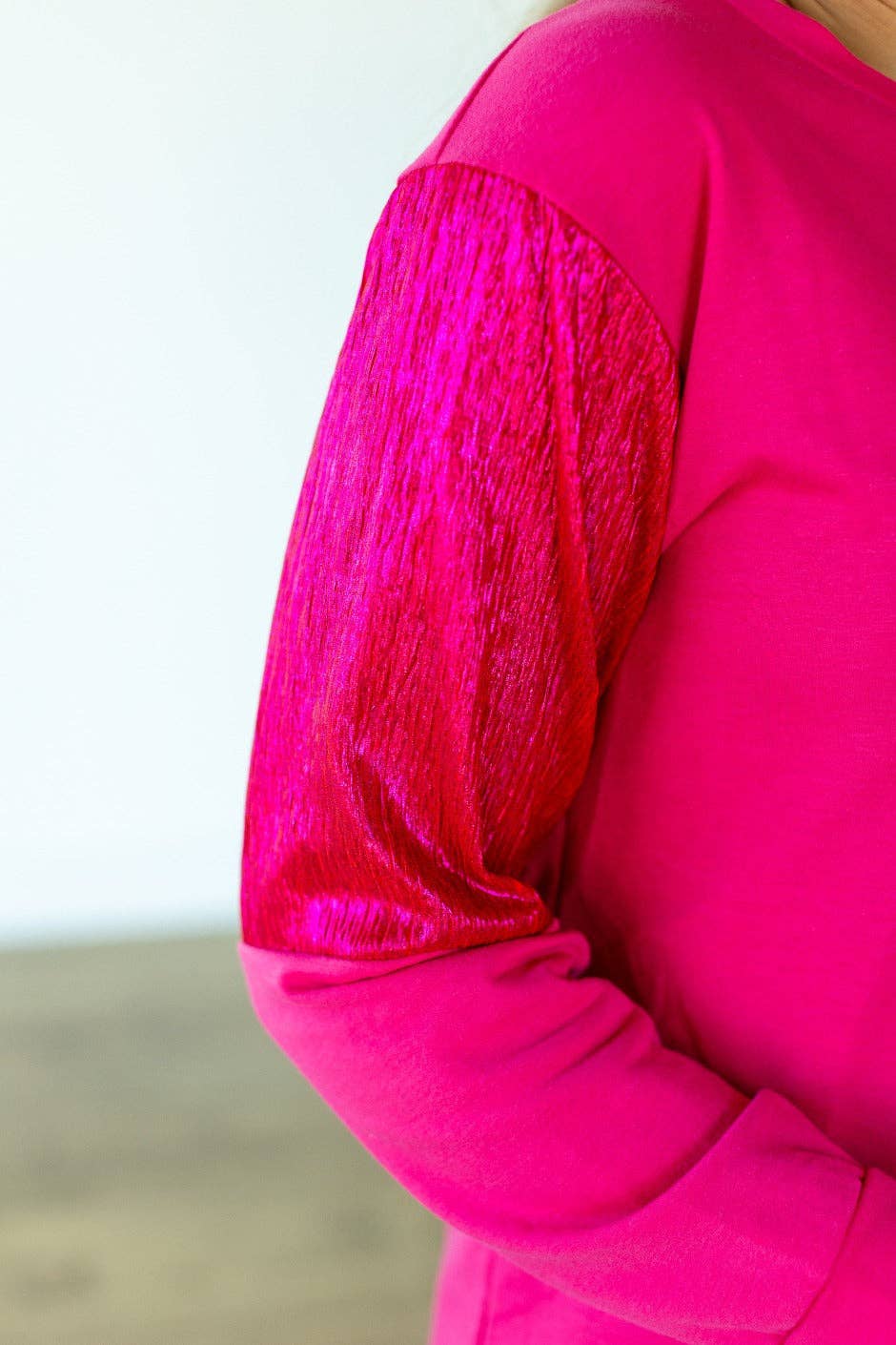 Close-up of a bright pink garment with textured sleeves against a neutral background