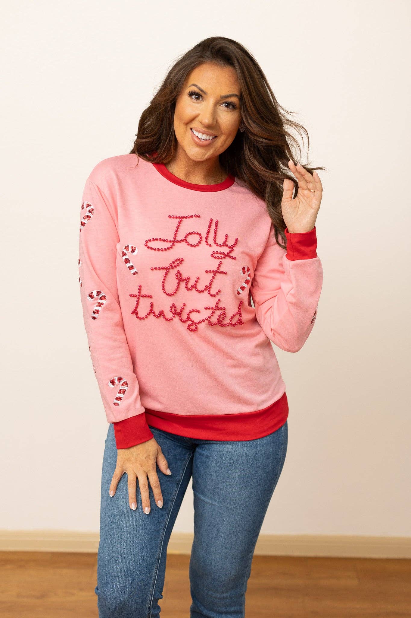 Woman smiling and modeling pink Jolly but Twisted holiday sweater with red trim and jeans