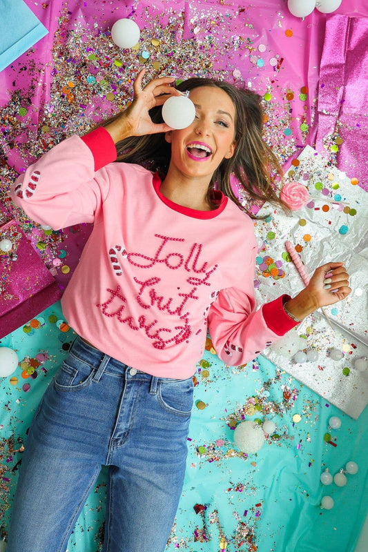 Model in Jolly but Twisted pink Christmas sweater lying on festive background with glitter and ornaments