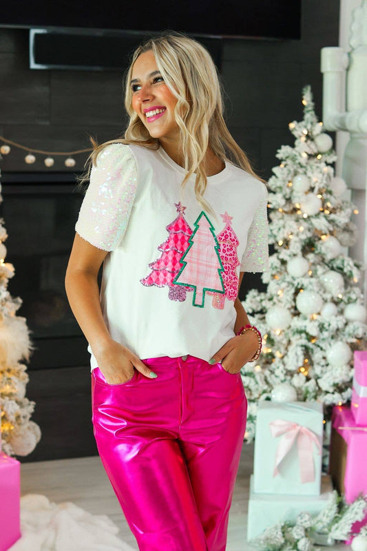 Woman wearing a white t-shirt with Christmas tree design and pink pants in a festive setting.