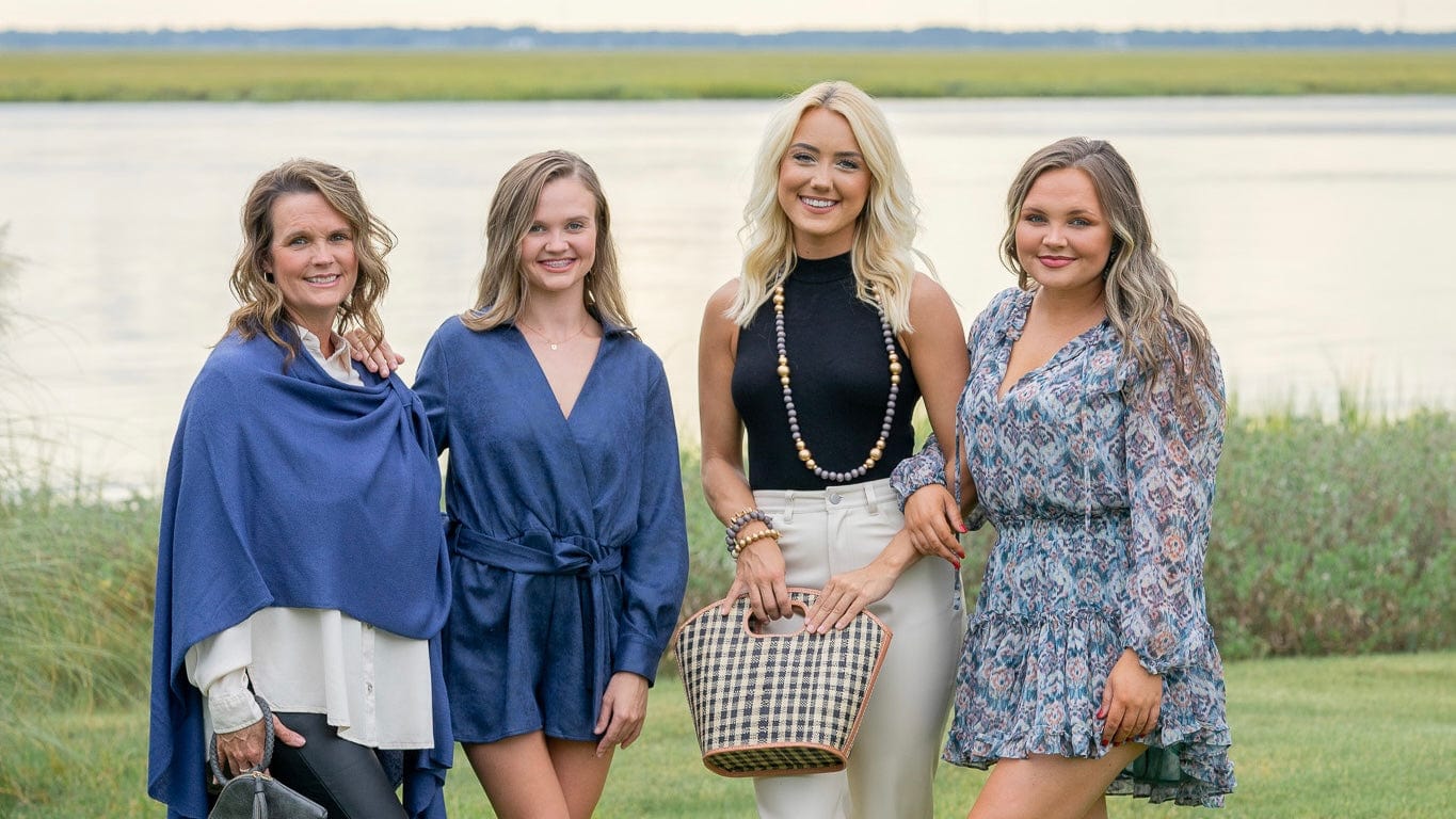 Four women posing together outdoors by a body of water.